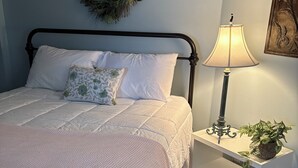 Un letto rifatto con lenzuola bianche, un comodino con una lampada e una ghirlanda appesa al muro.