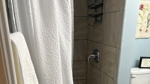 Un bagno con doccia, pareti piastrellate, un water e un certificato incorniciato appeso al muro.