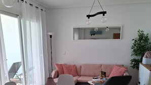 Un salon moderne avec une table de salle à manger ronde, des chaises blanches, un canapé rose et un fauteuil noir. On aperçoit une plante en pot et un meuble dans le coin.