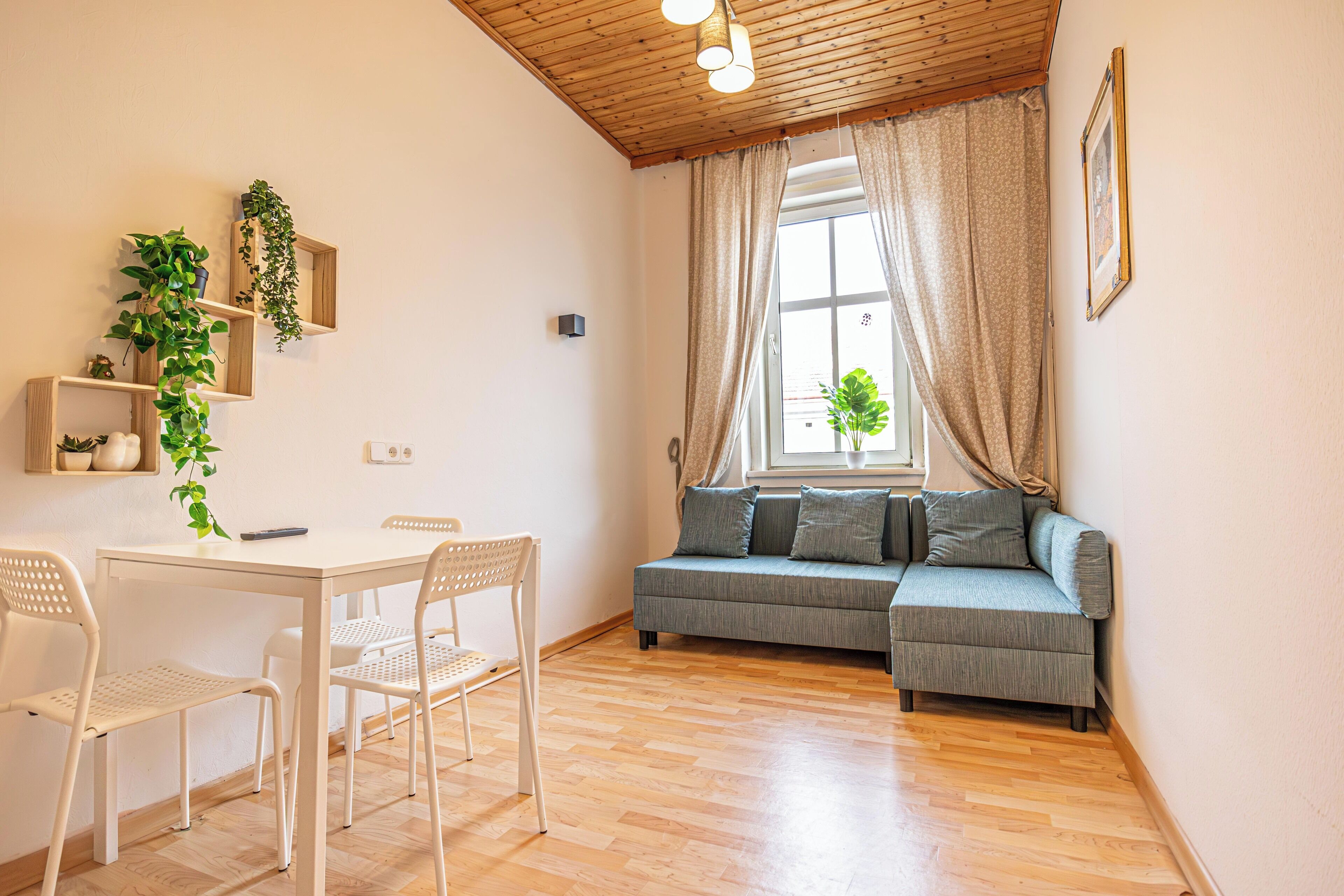 Une pièce avec un plafond en bois, un canapé, une table avec des chaises et une fenêtre avec des rideaux.