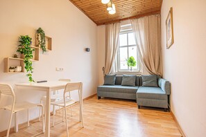 A room with a wooden ceiling, a sofa, a table with chairs, and a window with curtains. - Affordable Apartment Close to Stadthalle (Vienna)