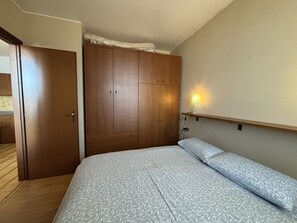 A bedroom with a bed, wooden wardrobe, and a wall-mounted lamp. - Graziella 1 Apartment with a View of the Lake (Germignaga)