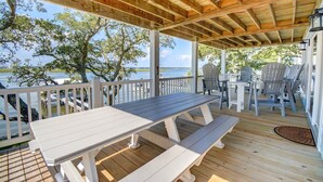 A covered outdoor deck with a wooden table and benches, overlooking a body of water and trees.