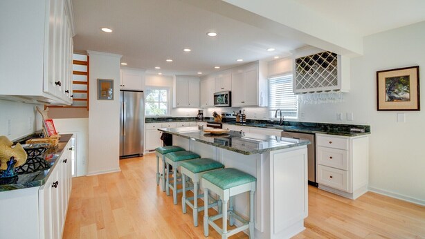 A modern kitchen with white cabinetry, a central island with bar stools, a stainless steel refrigerator, and a microwave.