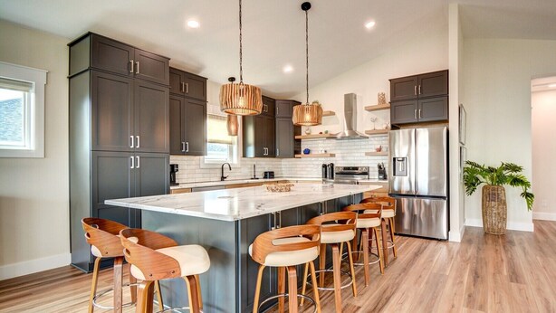 Una cocina moderna con armarios oscuros, una isla central con taburetes de bar, electrodomésticos de acero inoxidable y una lámpara colgante.