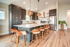 A modern kitchen with dark cabinets, a central island with bar stools, stainless steel appliances, and a hanging light fixture. - Experience luxury at Fin & Tonic, a 4-bedroom house with ocean views in North Topsail Beach. (North Topsail Beach)
