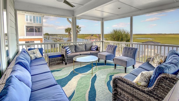 A covered outdoor seating area with a view of the water and a building in the background. - Explore Surf City from this spacious 6-bedroom, canal-front home, perfect for families. (Surf City)