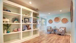 A spacious room with a wooden floor, white shelving units, and two armchairs. - Explore Surf City from this spacious 6-bedroom, canal-front home, perfect for families. (Surf City)