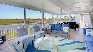 A covered outdoor area with seating, a glass table, and a view of the water and buildings. - Explore Surf City from this spacious 6-bedroom, canal-front home, perfect for families. (Surf City)