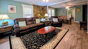A living room with a brown leather sofa, a wooden coffee table, a patterned rug, a stone accent wall, and a ceiling fan. - 3BR House with BBQ & Fire pit, Bryson City (Bryson City)
