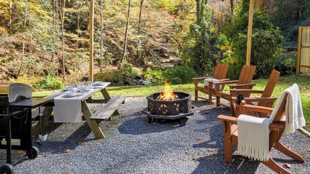 An outdoor patio with a fire pit, wooden chairs, a table set for dining, and a grill. - 3BR House with BBQ & Fire pit, Bryson City (Bryson City)