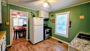 A kitchen with green walls, wooden flooring, a white refrigerator, a stove, and a dining area with chairs and a table. - 3BR House with BBQ & Fire pit, Bryson City (Bryson City)