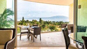 A balcony with a table and chairs, a glass door, and a view of the sea and mountains. - ANANA El Dorado 203 Condo with Lake views & Pool (Chapala)