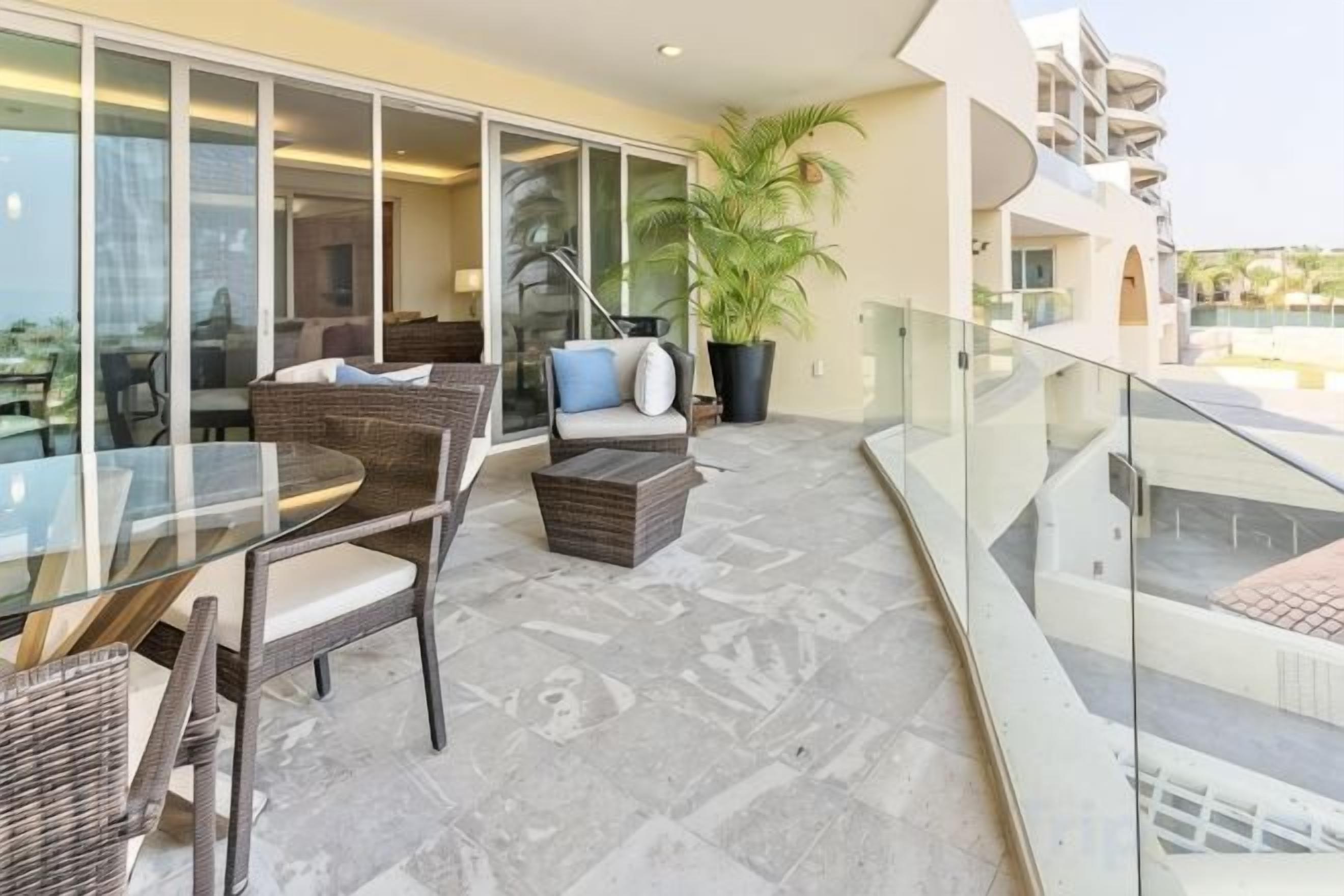 A balcony with wicker furniture, a glass table, and a potted plant.