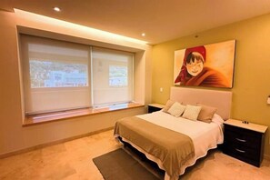 Een slaapkamer met een bed, nachtkastjes, een raam met zonwering en een schilderij aan de muur.