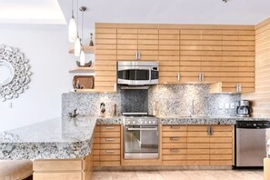 Een moderne keuken met houten kasten, granieten aanrecht en roestvrijstalen apparatuur, verlicht met hanglampen.