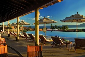 A poolside area with lounge chairs, umbrellas, and a view of a body of water and mountains.