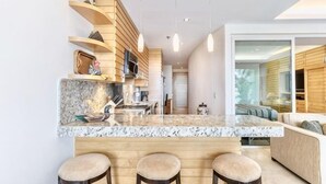 A modern kitchen with a marble countertop, wooden bar stools, pendant lights, and a view into the living area. - ANANA El Dorado 203 Condo with Lake views & Pool (Chapala)