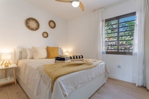 Un dormitorio con cama, mesitas de noche, ventilador de techo y ventana con vistas.