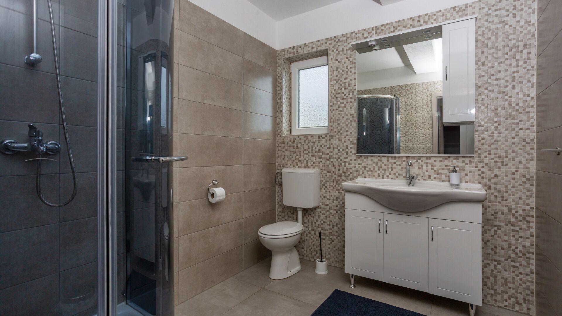 A modern bathroom with a glass shower enclosure, a toilet, and a sink with a mirror above it.
