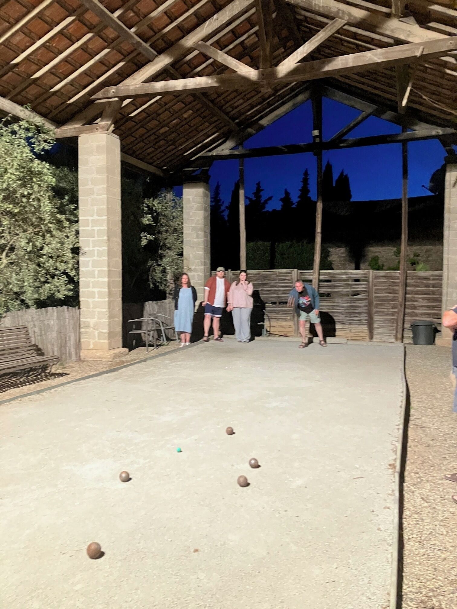 A covered outdoor area with a concrete floor, a wooden bench, and a stone pillar.