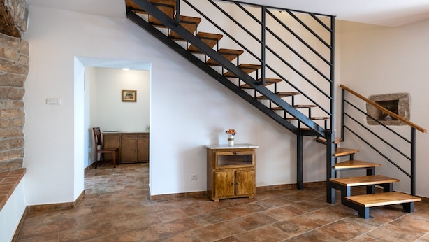 Een trap met houten treden en zwarte metalen leuningen, die leidt naar een ruimte met een stenen muur en een houten kast.