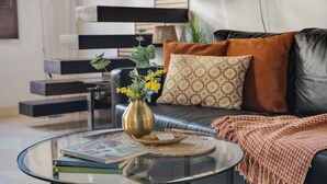 Uma sala de estar moderna com uma mesa de centro de vidro, livros, um vaso decorativo e um sofá com almofadas estampadas.