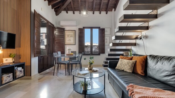 Uma sala de estar moderna com mesa de centro de vidro, sofá de couro, painéis de parede de madeira e uma escada.