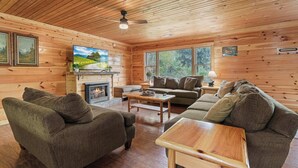 A cozy cabin interior with wooden walls, a fireplace, a television, and a large window offering a view of the outdoors. - 10.3 Mi to Dollywood・Cozy Cabin Stay・Hot Tub・Games (Sevierville)