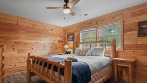 A wooden-paneled bedroom with a bed, a nightstand, a lamp, and a window. - 10.3 Mi to Dollywood・Cozy Cabin Stay・Hot Tub・Games (Sevierville)