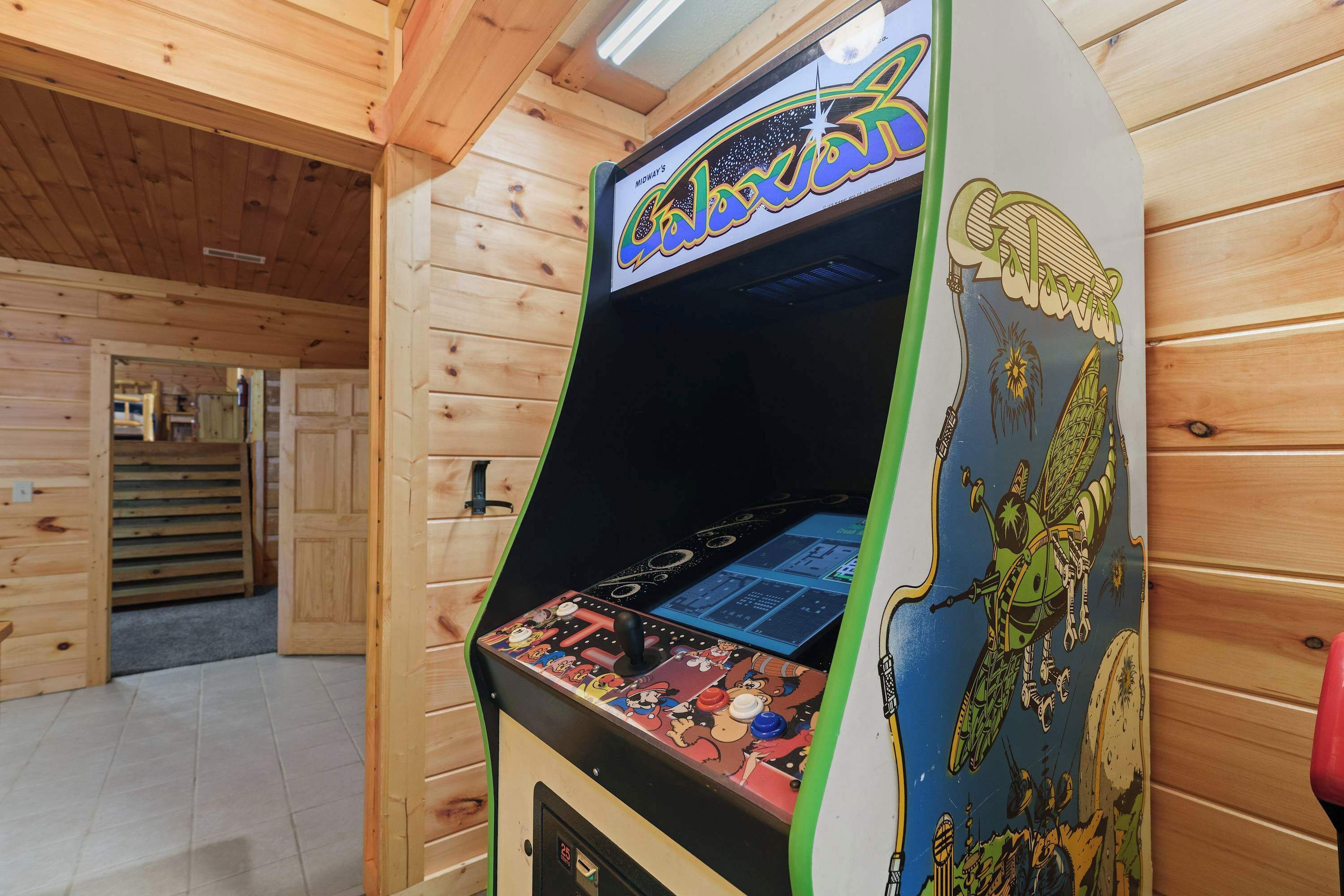 An arcade machine with a space-themed design, located in a wooden room with a sloped ceiling.