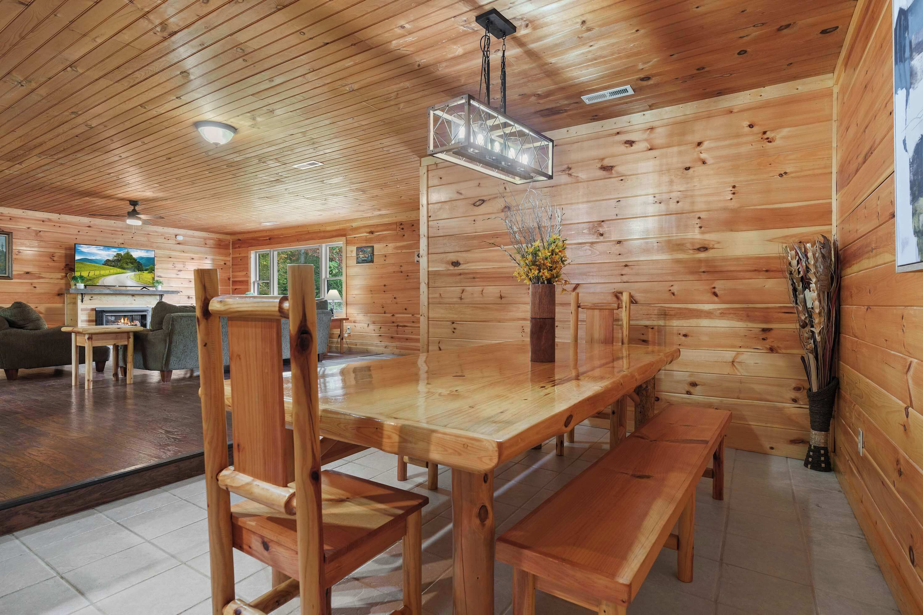 A wooden interior with a dining table, benches, a TV, and a fireplace.