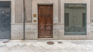 En byggnadsentré med en dubbel träport, ett stort fönster och ett plattlagt trottoar.
