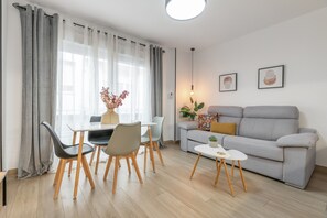 Ein modernes Wohnzimmer mit einem grauen Sofa, einem Esstisch mit Stühlen und einem kleinen Beistelltisch.