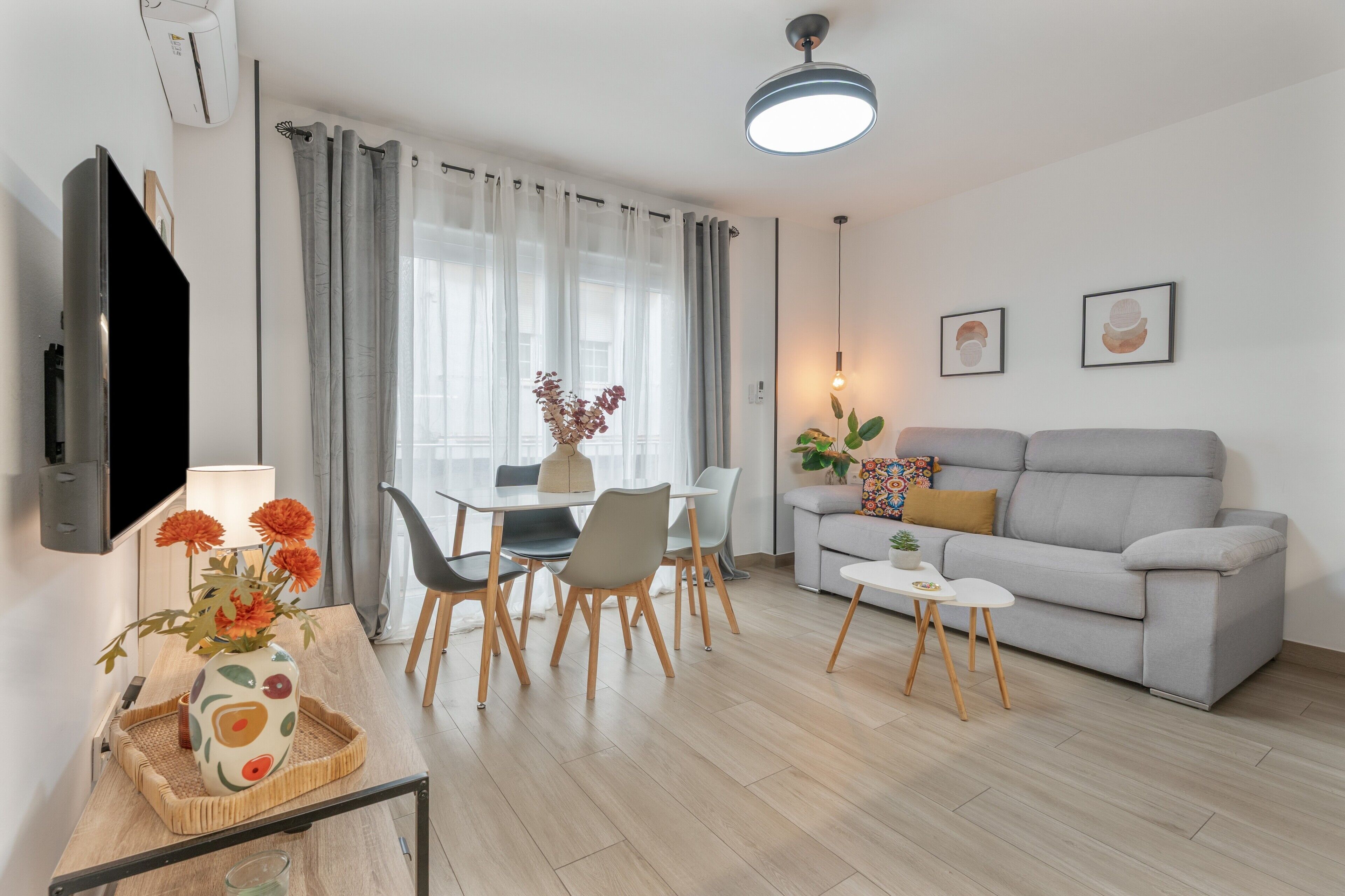 A modern living room with a sofa, dining table, chairs, and a TV.
