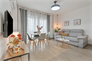Ein modernes Wohnzimmer mit einer Couch, einem Esstisch, Stühlen und einem Fernseher.