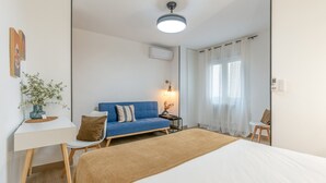 A bedroom with a bed, a blue sofa, a desk, a chair, a plant, and a window with curtains. - Apartment 'Apartamento Canasteros 12 Centro' with Balcony, Wi-Fi and Air Conditioning (Granada)