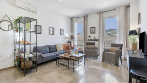 Un salon moderne comprenant un canapé, une table basse et un fauteuil, une bibliothèque et une grande fenêtre donnant sur un beau paysage.