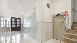 Un hall d’entrée propre et moderne, avec un sol en marbre, un escalier et une porte sur laquelle est apposé un panneau indiquant qu’il est interdit de fumer.