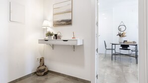 Une pièce propre et moderne, avec une console blanche, une lampe, une guitare, un tableau et un coin repas comprenant des chaises et une table.