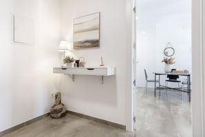 Ein sauberes, modernes Zimmer mit einem weißen Schminktischchen, einer Lampe, einer Gitarre, einem Gemälde und einem Essbereich mit Stühlen und einem Tisch.