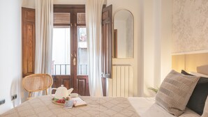 Ein Schlafzimmer mit einem Bett, einem Nachttisch mit Teekanne, einem Sessel und einem Fenster mit Vorhängen.