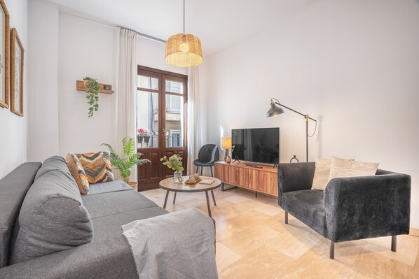 Ein modernes Wohnzimmer mit Sofa, Sessel, Fernseher und einem kleinen Tisch mit Dekoration.