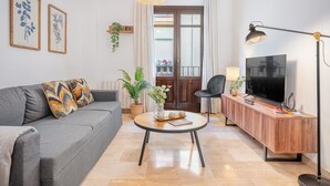Ein modernes Wohnzimmer mit grauem Sofa, rundem Couchtisch, Fernseher und Holzschrank.