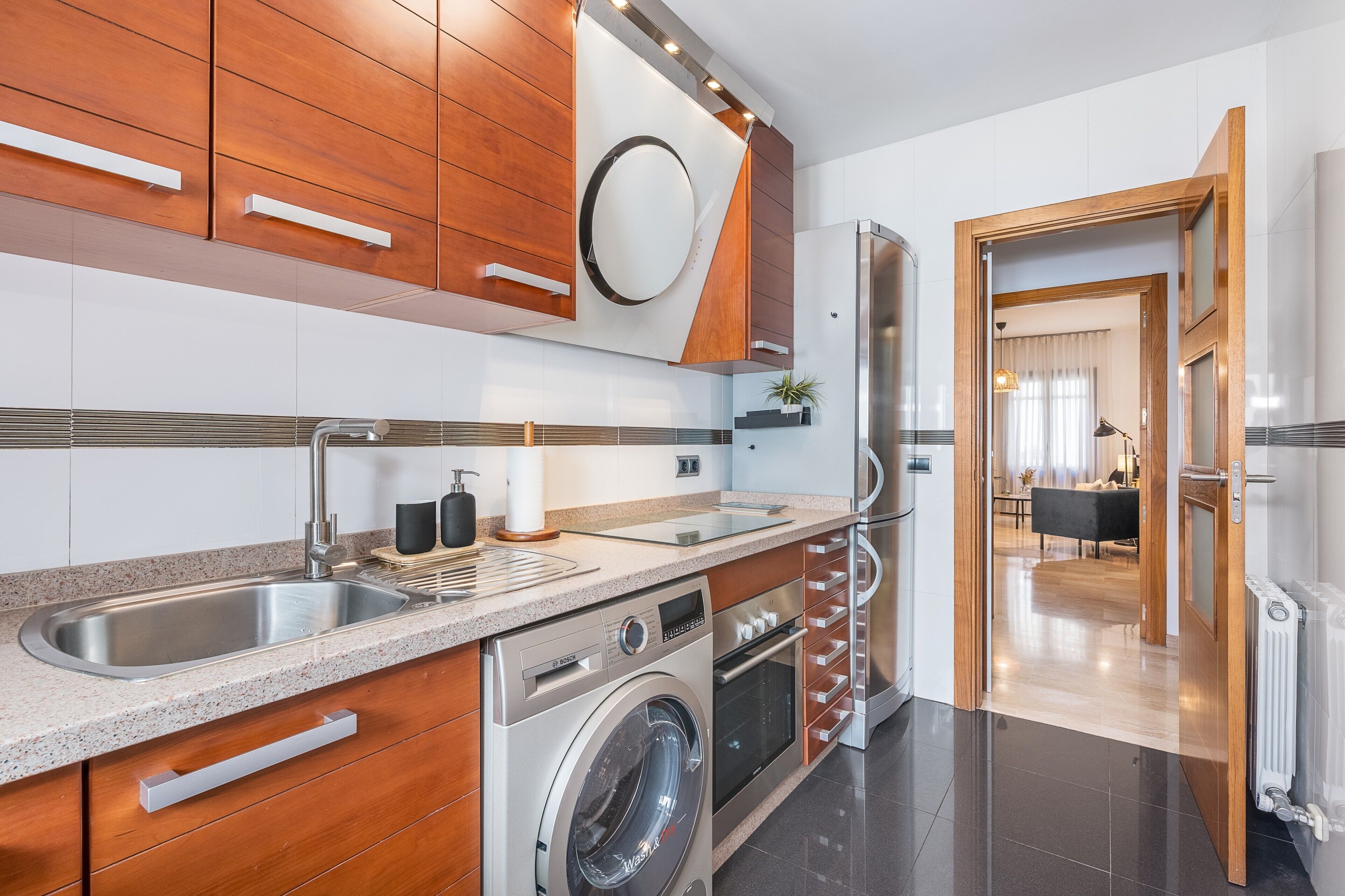 A modern kitchen with stainless steel appliances, wooden cabinets, and a built-in washing machine.
