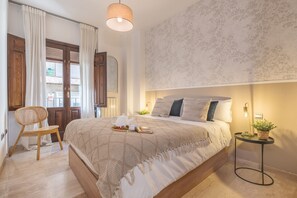Ein Schlafzimmer mit einem Bett, einem Sessel, einem Nachttisch mit Pflanze und einer Wand mit floralem Muster.