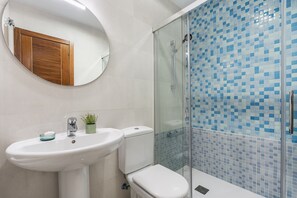 Ein Badezimmer mit weißem Waschbecken, Toilette, Duschkabine aus Glas und Spiegel.