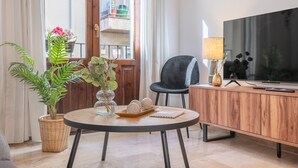 Ein modernes Wohnzimmer mit einem runden Tisch, einer Couch, einem Fernseher und Blick auf einen Balkon.
