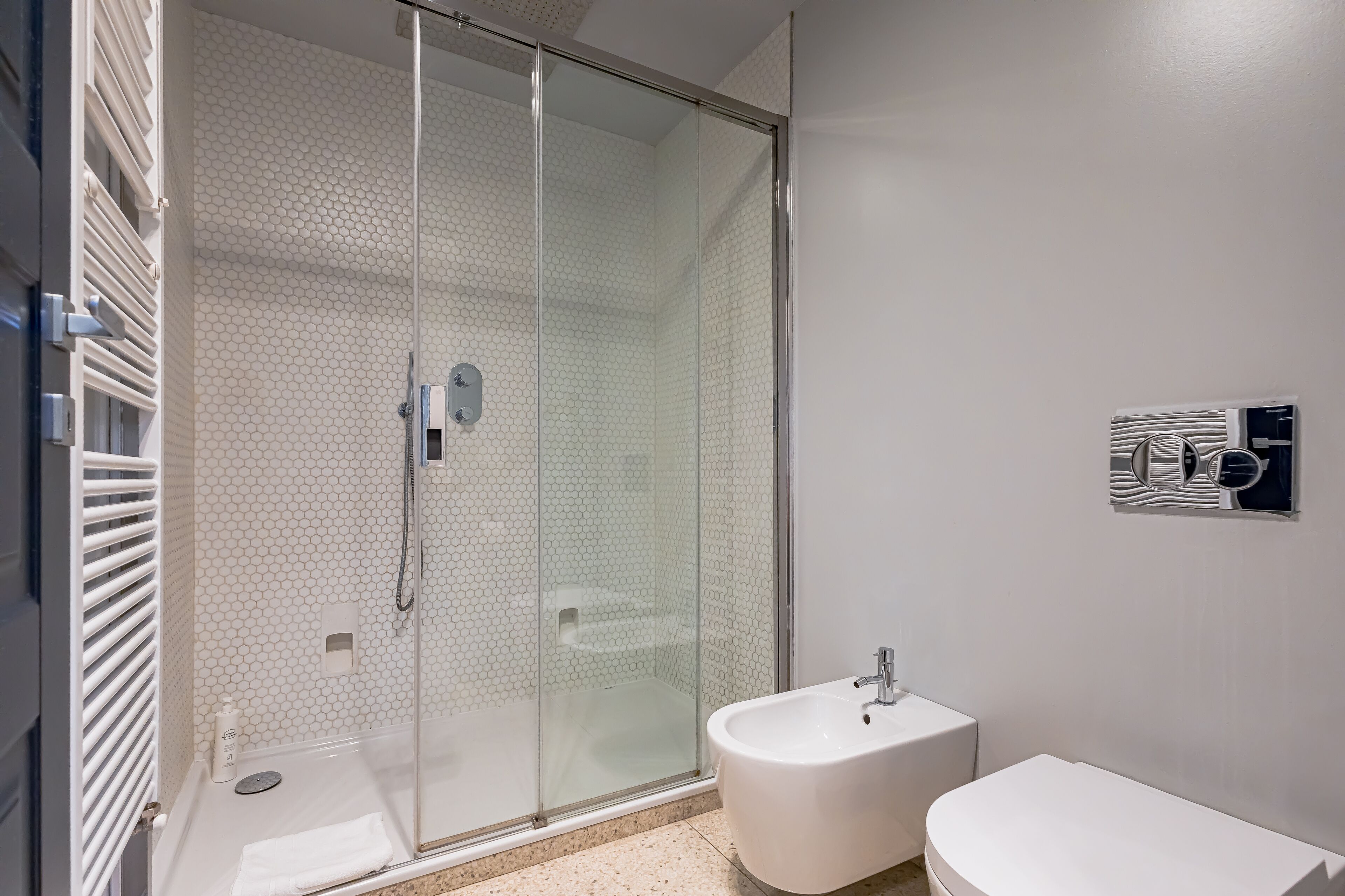 Een moderne badkamer met een douchecabine van glas, een wit wastafeltje en een toilet.