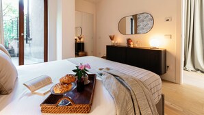 Ein Schlafzimmer mit einem großen Bett, einem Nachttisch mit einer Auswahl an Gebäck, einem Spiegel und Blick ins Freie.